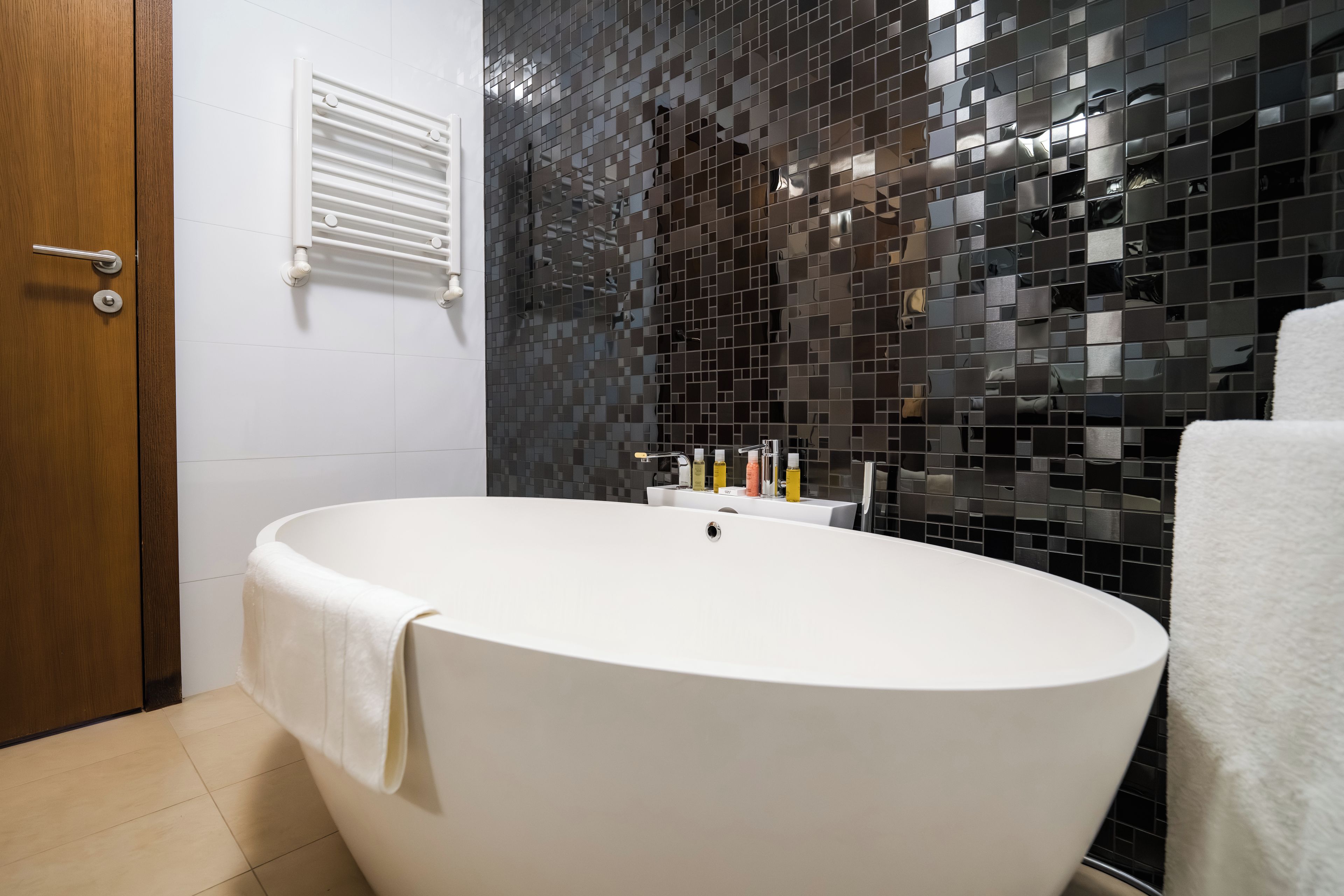 Un baño moderno con una bañera independiente, un perchero para toallas y un dispensador de toallas en la pared.