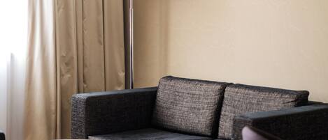 Una habitación de hotel moderna con un sofá gris, una mesa redonda, una lámpara de pie y un cuadro enmarcado en la pared.