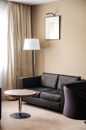 A modern hotel room with a grey sofa, a round table, a floor lamp, and a framed picture on the wall. - Mikado Hotel (Nitra)