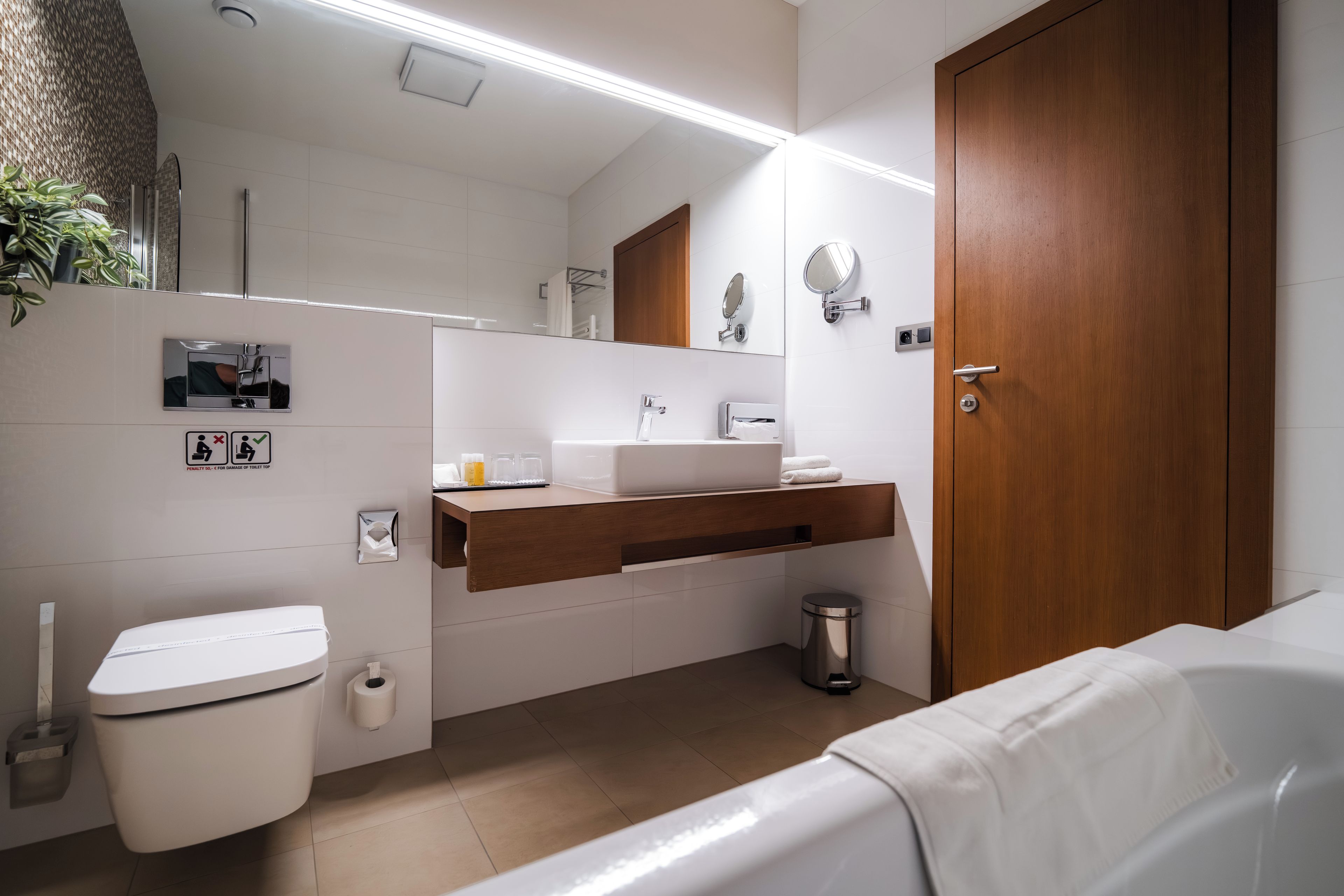 Ein modernes Badezimmer mit Toilette, Waschbecken, Spiegel und einer Holztür.