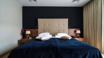 A hotel room with a large bed, two bedside tables, a headboard, and a window with curtains.