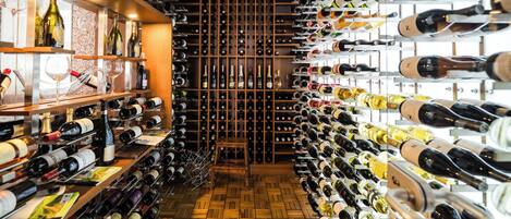 A wine cellar with rows of wine bottles on shelves and racks, wooden flooring, and a central aisle.