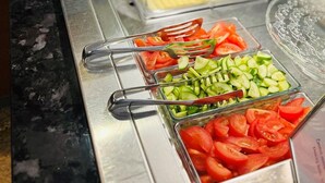 Un bufé con diversas opciones de comida, incluyendo tomates en rodajas, pepinos y otras verduras.