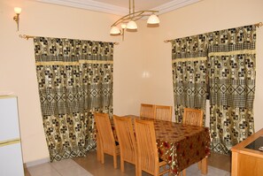 A dining area with a table and chairs, patterned curtains, and a chandelier.