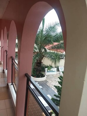A corridor with arched ceilings and a view of a palm tree and a building with a red roof.