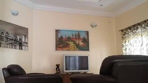 Una sala de estar con dos sofás marrón oscuro, un televisor de pantalla plana, un ventilador de techo y dos cuadros colgados en la pared.