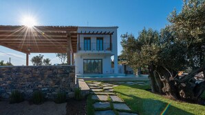 A modern two-story house with a stone wall, a wooden pergola, and a stone pathway leading to the entrance. - Stargaze Villas (Skopelos)