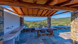 An outdoor patio with a wooden pergola, stone walls, a built-in sink, and a table with chairs. - Stargaze Villas (Skopelos)