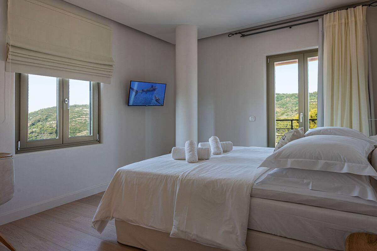 A hotel room with a bed, a TV, and a balcony with curtains.