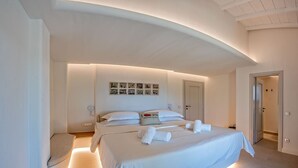 A modern bedroom with a large bed, a bedside table, a wall-mounted clock, and a door. - Stargaze Villas (Skopelos)