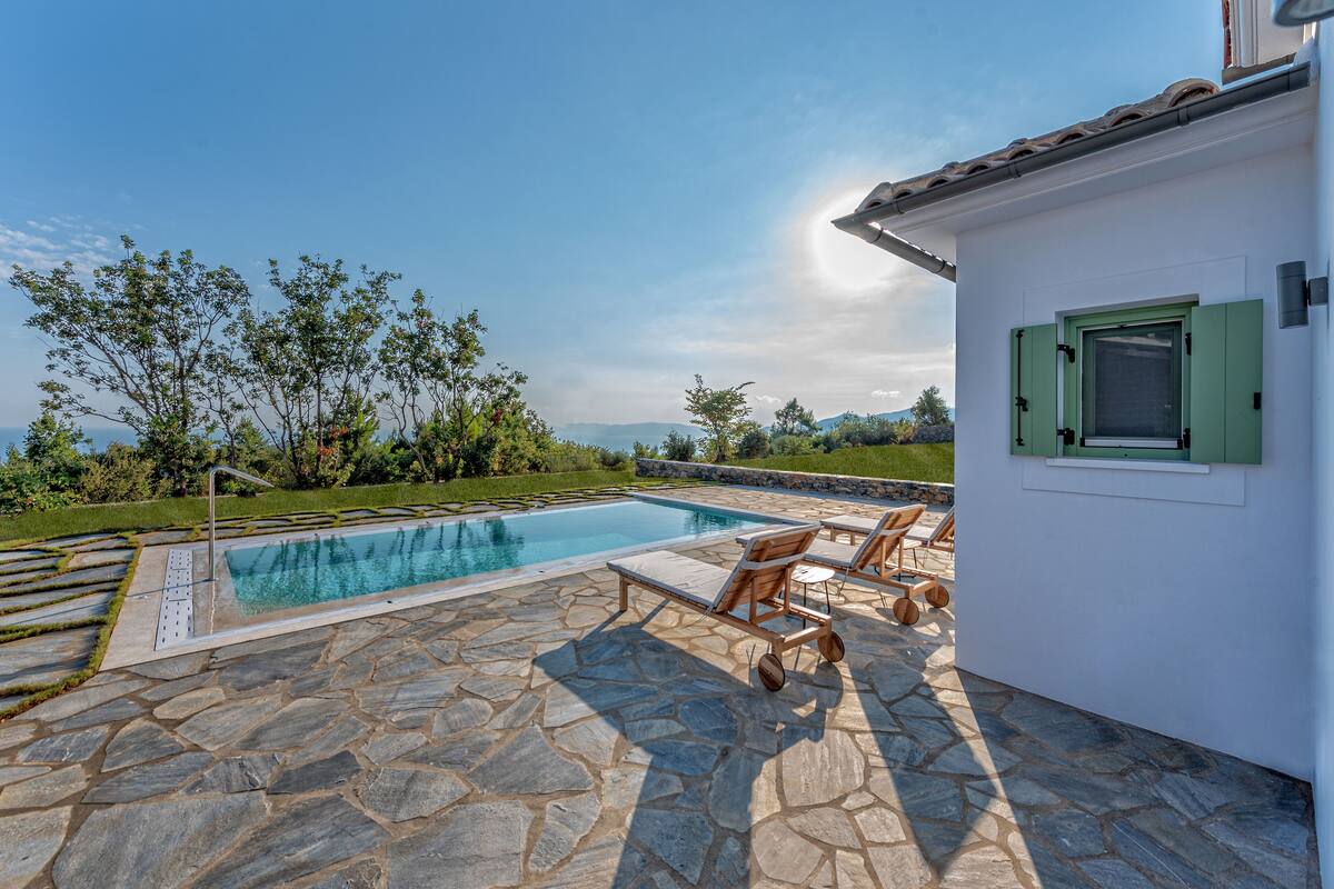 A stone patio with a pool, outdoor furniture, and a view of the landscape.