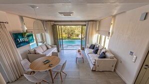 A spacious living area with a large TV, a dining table, and a sofa. - Stargaze Villas (Skopelos)