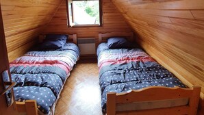 A cozy attic bedroom with wooden walls and a sloped ceiling, featuring two beds with star-patterned bedding and a small window providing natural light. - Chalet between lakes and mountains, unlimited fishing (Beaulieu)