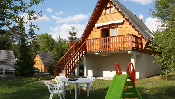 A wooden cabin with a balcony, a slide, and a table with chairs in the yard. - Chalet between lakes and mountains, unlimited fishing (Beaulieu)