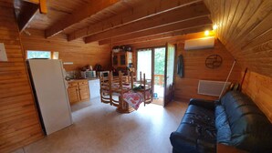 A wooden cabin interior with a dining area, kitchen, and a blue sofa. - Chalet between lakes and mountains, unlimited fishing (Beaulieu)