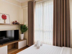 A hotel room with a bed, a TV on a wooden stand, a potted plant, and a window with curtains.