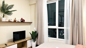 Hotellihuone, jossa on sänky, puinen tv-taso, ruukkukasvi ja ikkuna, jossa on verhot.