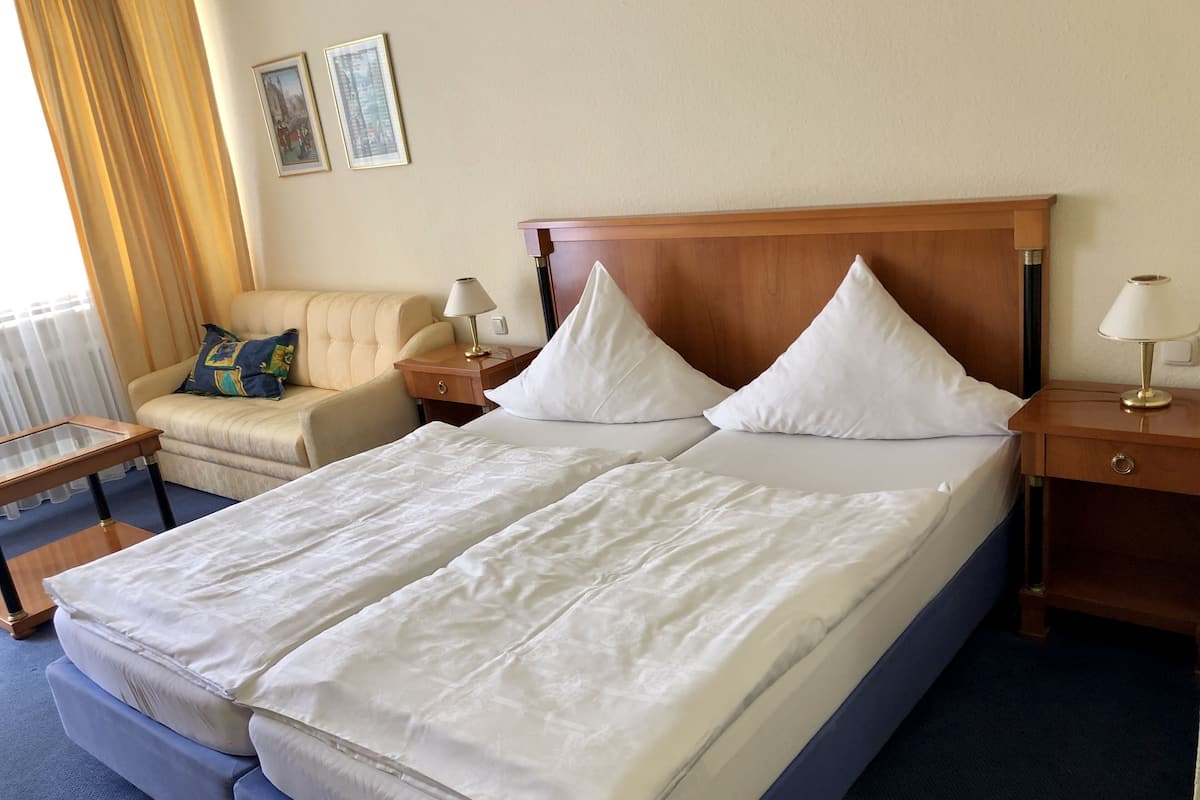 A hotel room with a double bed, a sofa, a nightstand with a lamp, and a small table.