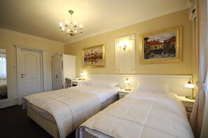 Habitación de hotel con dos camas, una araña, lámparas de pared y dos cuadros.