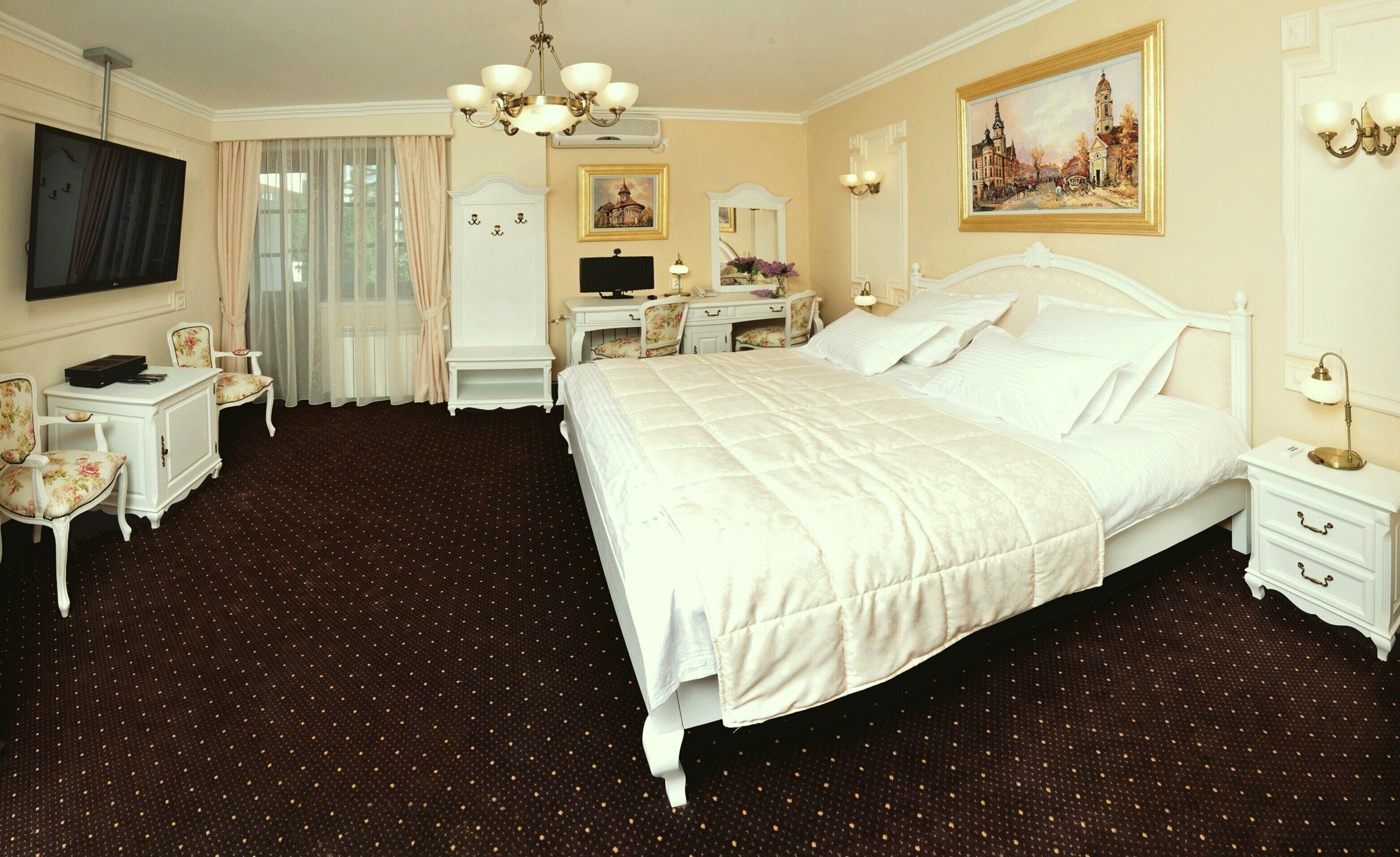 A hotel room with a large bed, a desk, a chair, a television, and a painting on the wall.