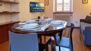 A dining area with a round table set for four, surrounded by chairs. There is a television mounted on the wall displaying a streaming service interface.