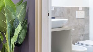A modern bathroom with a white sink, two toilets, and a large green plant. - Precious Room with Private bathroom ★Prussian Blue ★Free Wifi (Trieste)