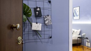 A room with a wooden door, a wall-mounted grid with framed pictures, a white bed with pillows, and a small side table. - Precious Room with Private bathroom ★Prussian Blue ★Free Wifi (Trieste)