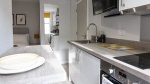 A modern kitchen with a built-in microwave, a stainless steel range hood, and a dishwasher. - Spa Court (Cheltenham)