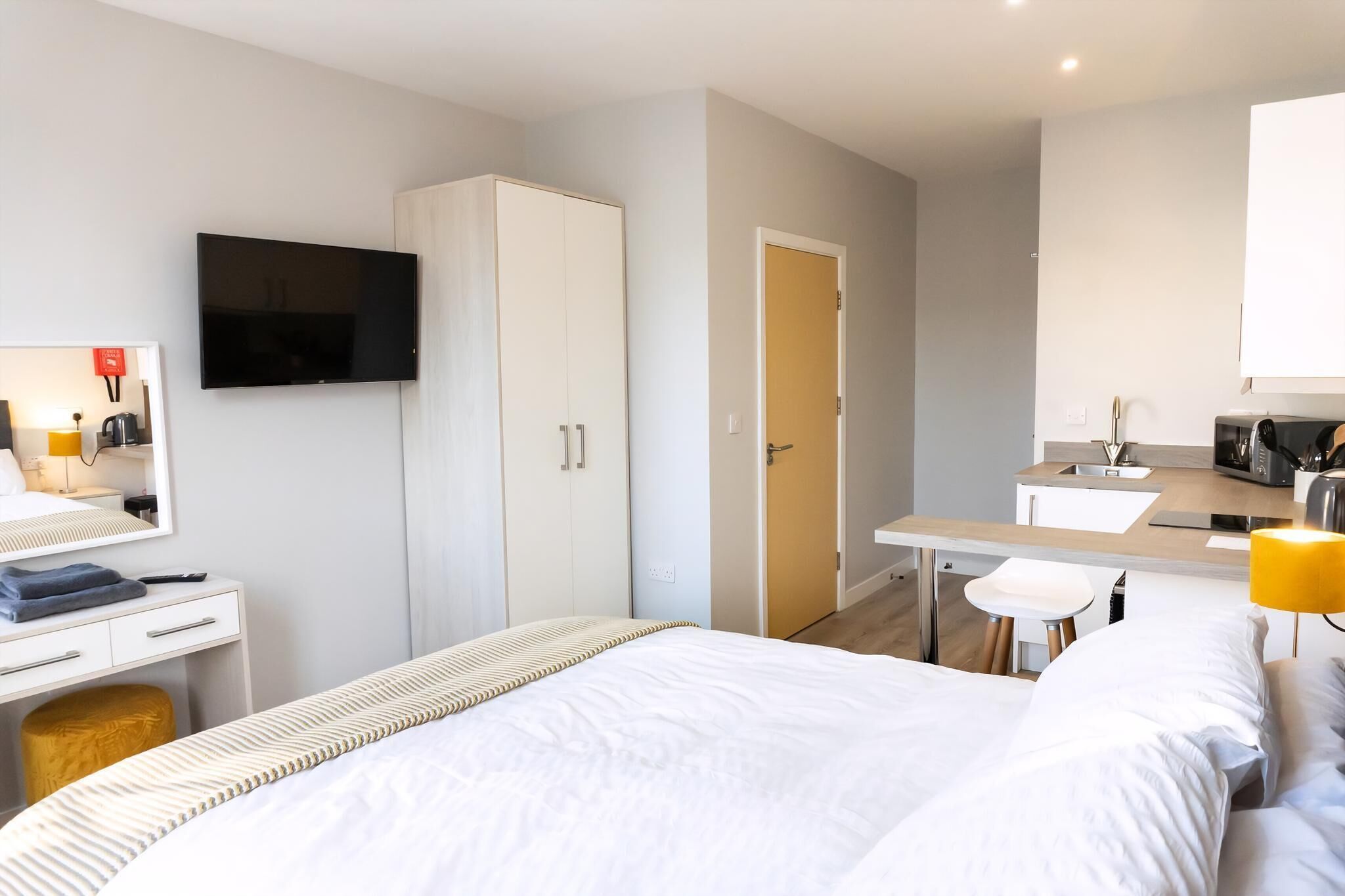 Habitación de hotel con cama, escritorio, televisión, armario, kitchenette y baño.