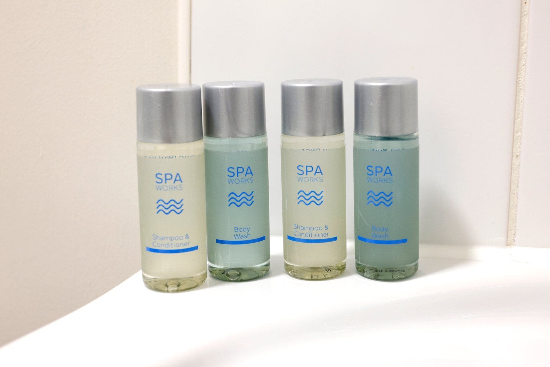 Quatre bouteilles de gel douche et de shampoing de la marque SPA WORKS, posées sur une surface blanche.