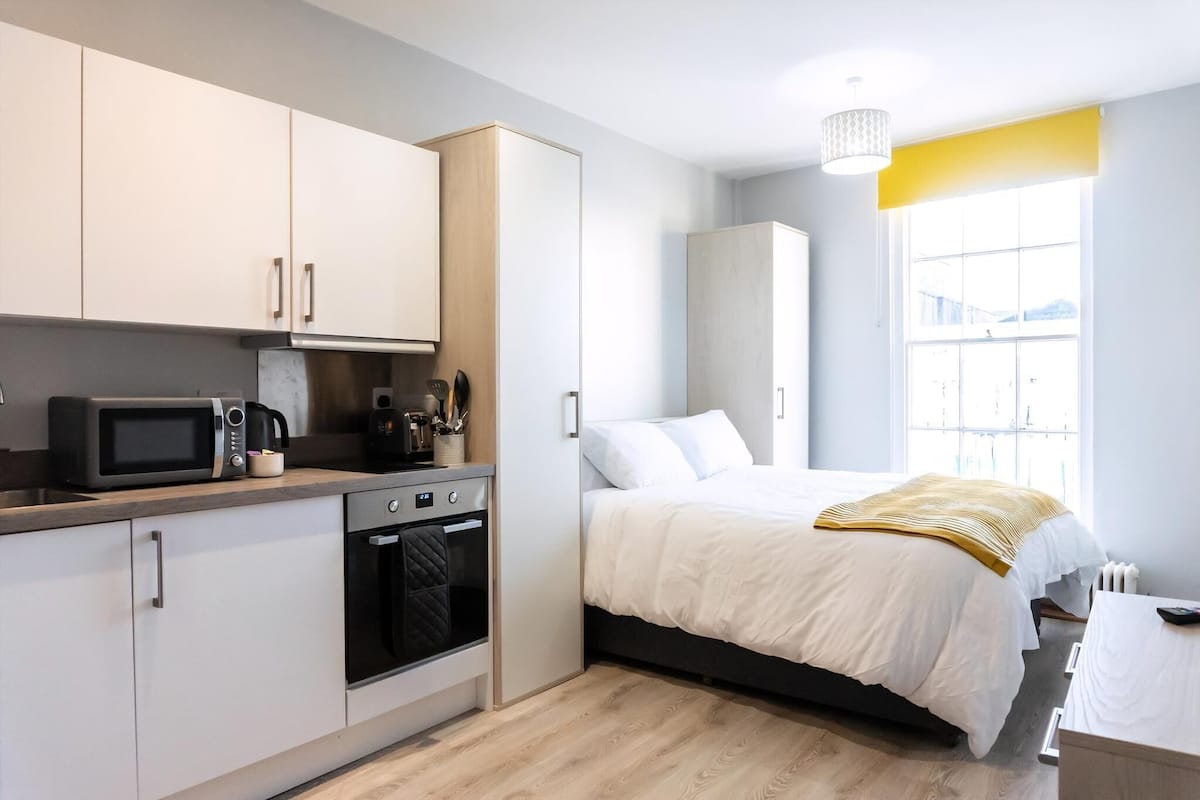 A compact room with a kitchenette, a bed, and a window.