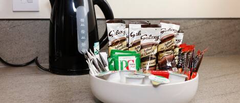 A kitchen counter with a black kettle, a bowl of instant coffee packets, and a coffee grinder.