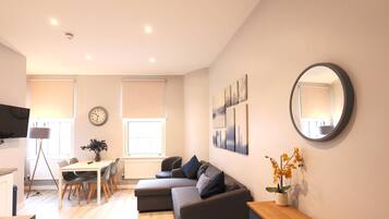 Ein modernes Wohnzimmer mit einer Couch, einem Esstisch mit Stühlen, einer Uhr und Bildern an den Wänden.