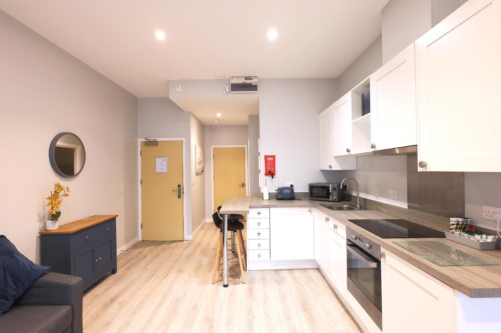 Een moderne keuken met een magnetron, fornuis en een spoelbak. Er is een klein zitehoekje met een tafel en stoelen.