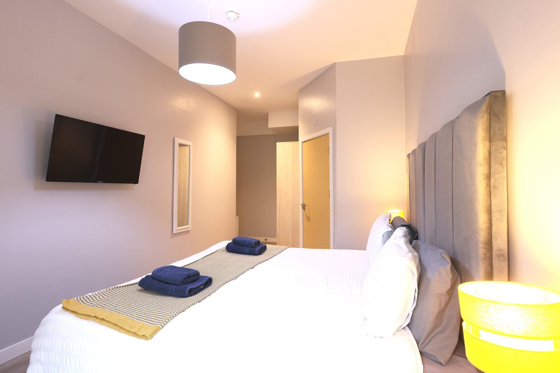 A hotel room with a bed, a flat-screen TV, a bedside lamp, and a door leading to another room.