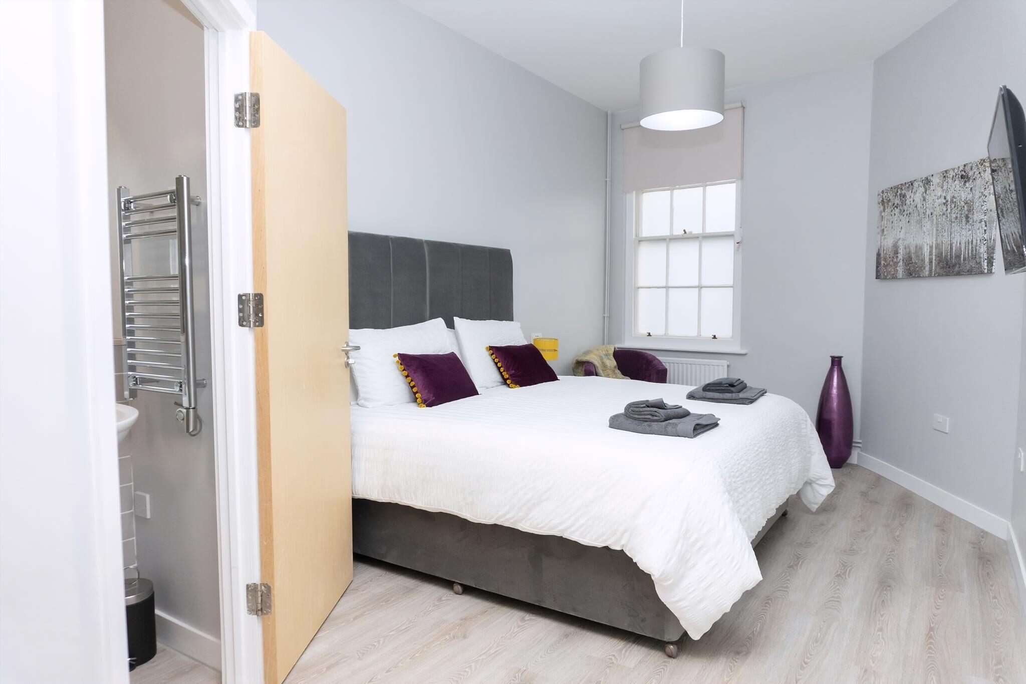 Ein Schlafzimmer mit Bett, Nachttisch, Fenster und einem Kunstwerk an der Wand.