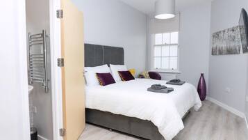 Ein Schlafzimmer mit Bett, Nachttisch, Fenster und einem Kunstwerk an der Wand.
