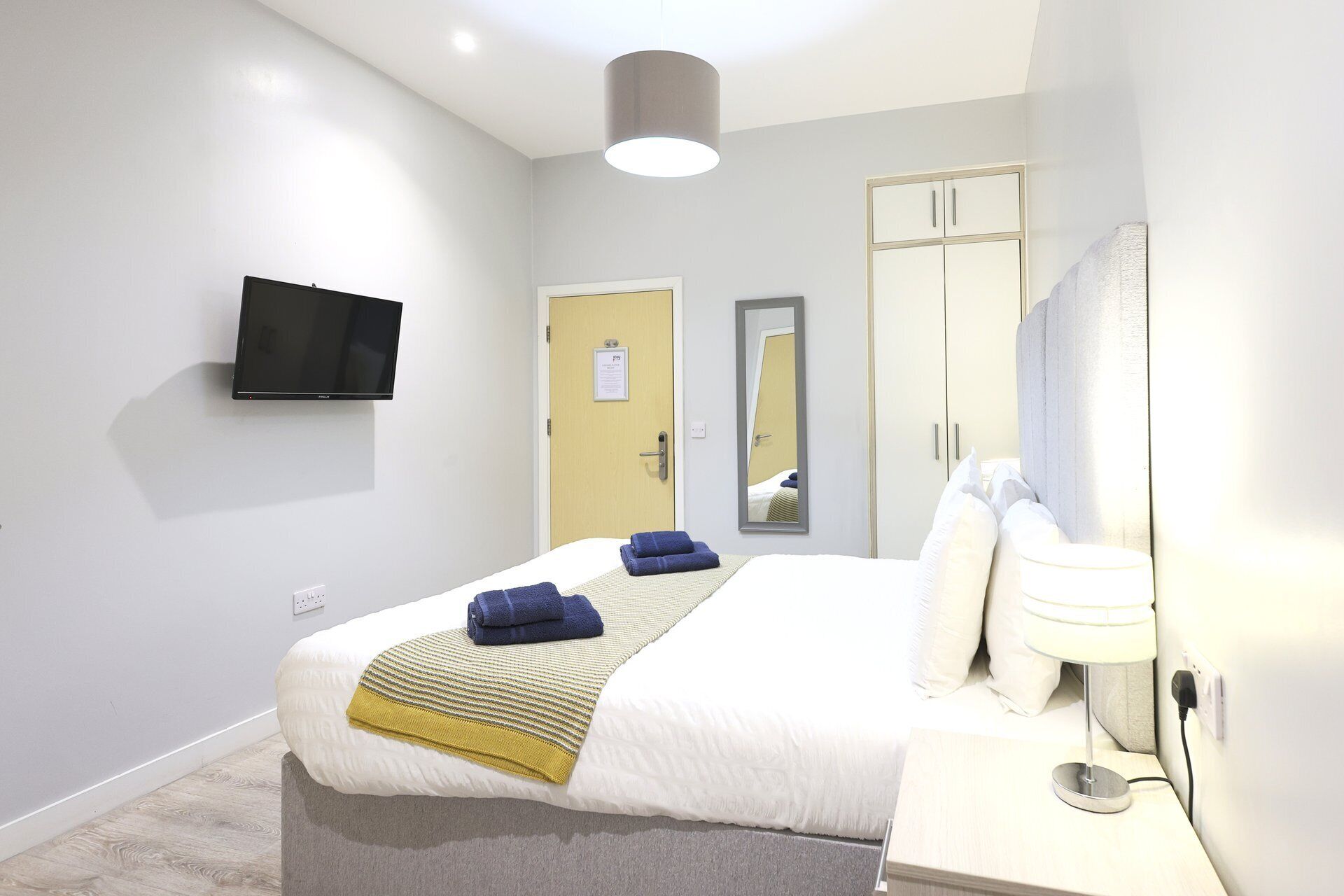 Ein Hotelzimmer mit Bett, Wandfernseher, Kleiderschrank und Spiegel.