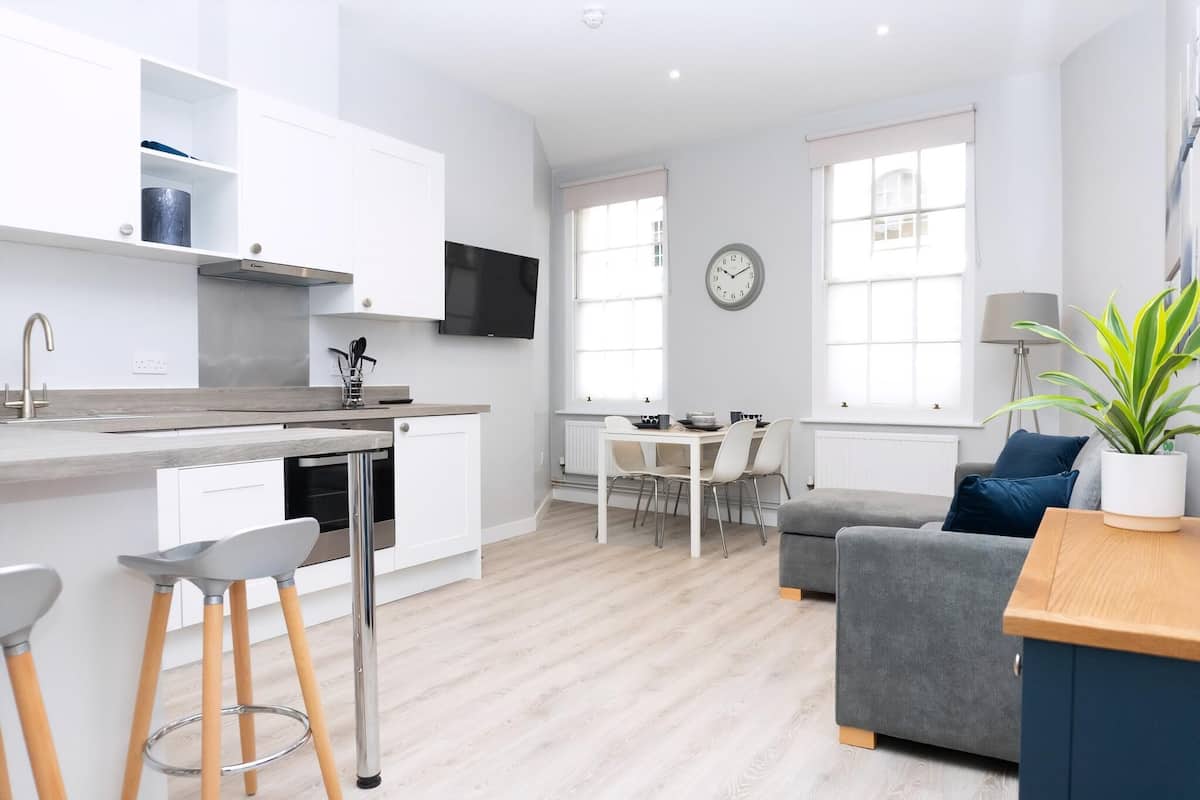 A modern kitchen with white cabinetry, a flat-screen TV, and a dining area with a table and chairs.