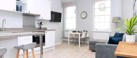 A modern kitchen with white cabinetry, a flat-screen TV, and a dining area with a table and chairs.