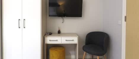 A room with a white desk, a black chair, a television mounted on the wall, and a wooden floor.