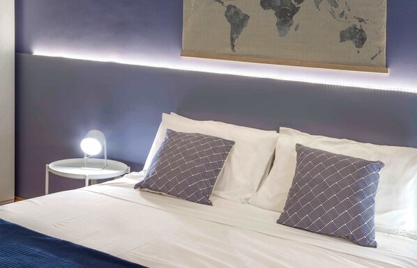 Un lit bien fait, agrémenté de deux coussins à motifs, une table de chevet avec une lampe et une carte du monde accrochée au mur.