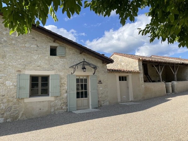A stone building with a gravel driveway, a wooden staircase, and a tiled roof.