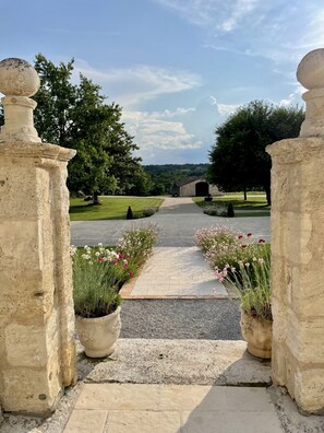 A stone pathway leading to a building with a covered entrance, surrounded by greenery and a clear sky.