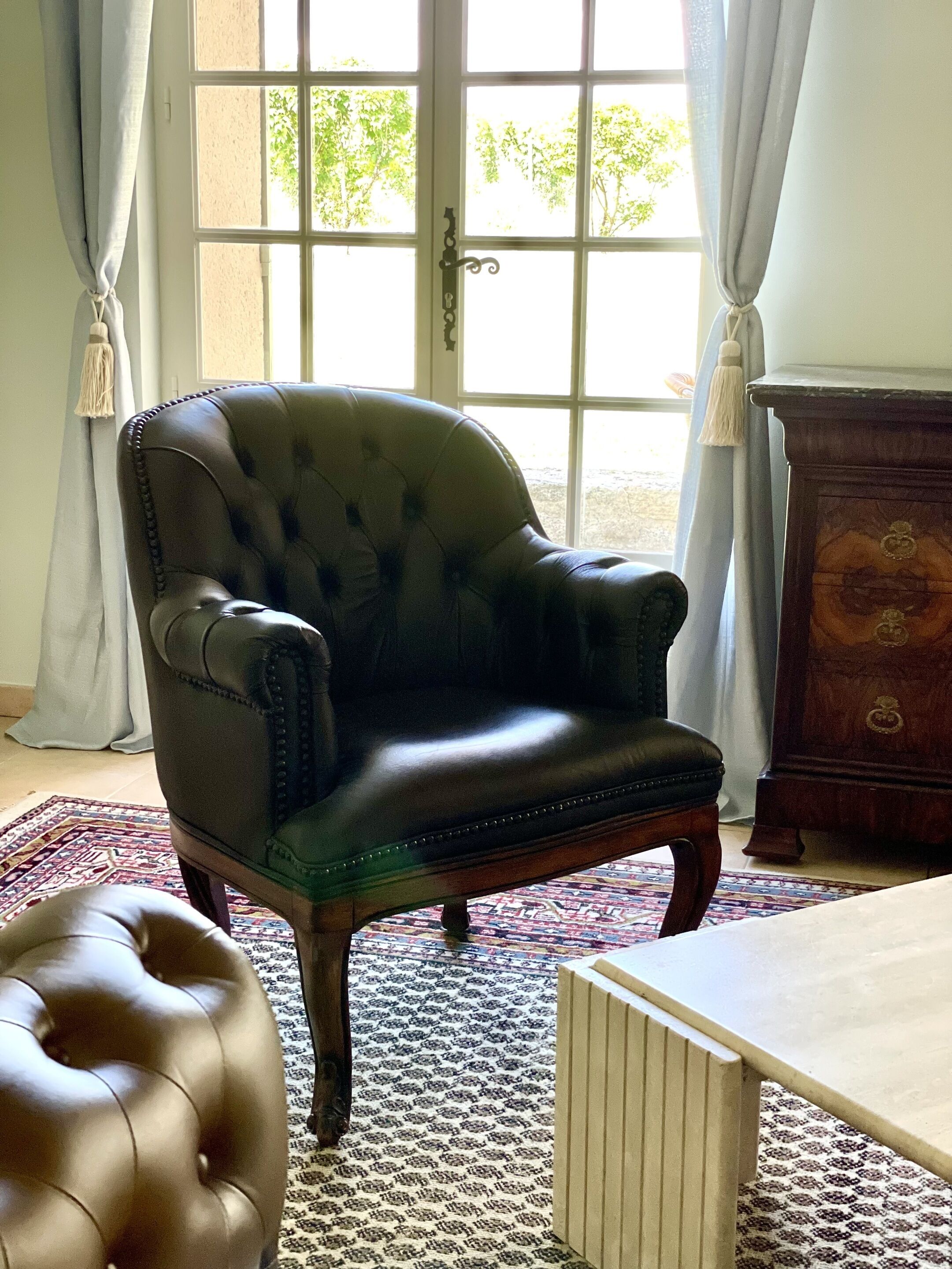 Ein Zimmer mit Ledersessel, Holzschrank und einem gemusterten Teppich.