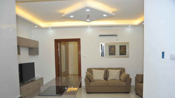 Una sala de estar moderna con una televisión de pantalla plana, un sofá color beige y una mesa de centro de vidrio.