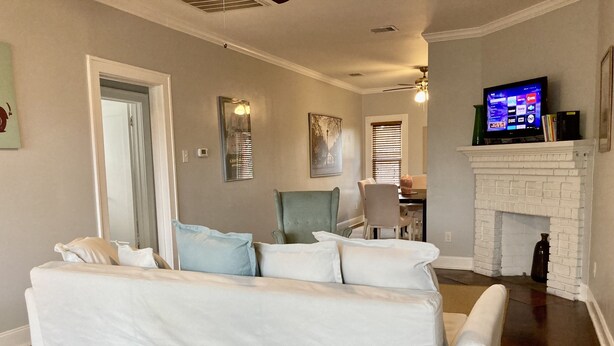 A living room with a white sofa, a fireplace, a television, and a dining area in the background.