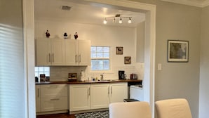 A kitchen with white cabinets, a stove, and a window. There are two chairs and a table in the dining area.