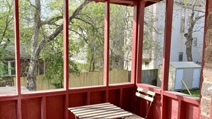 A covered patio with a wooden table and benches, large windows, and a view of trees and a house.
