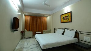 Habitación de hotel con cama, televisión, ventilador de techo, un cuadro y ventana con cortinas.